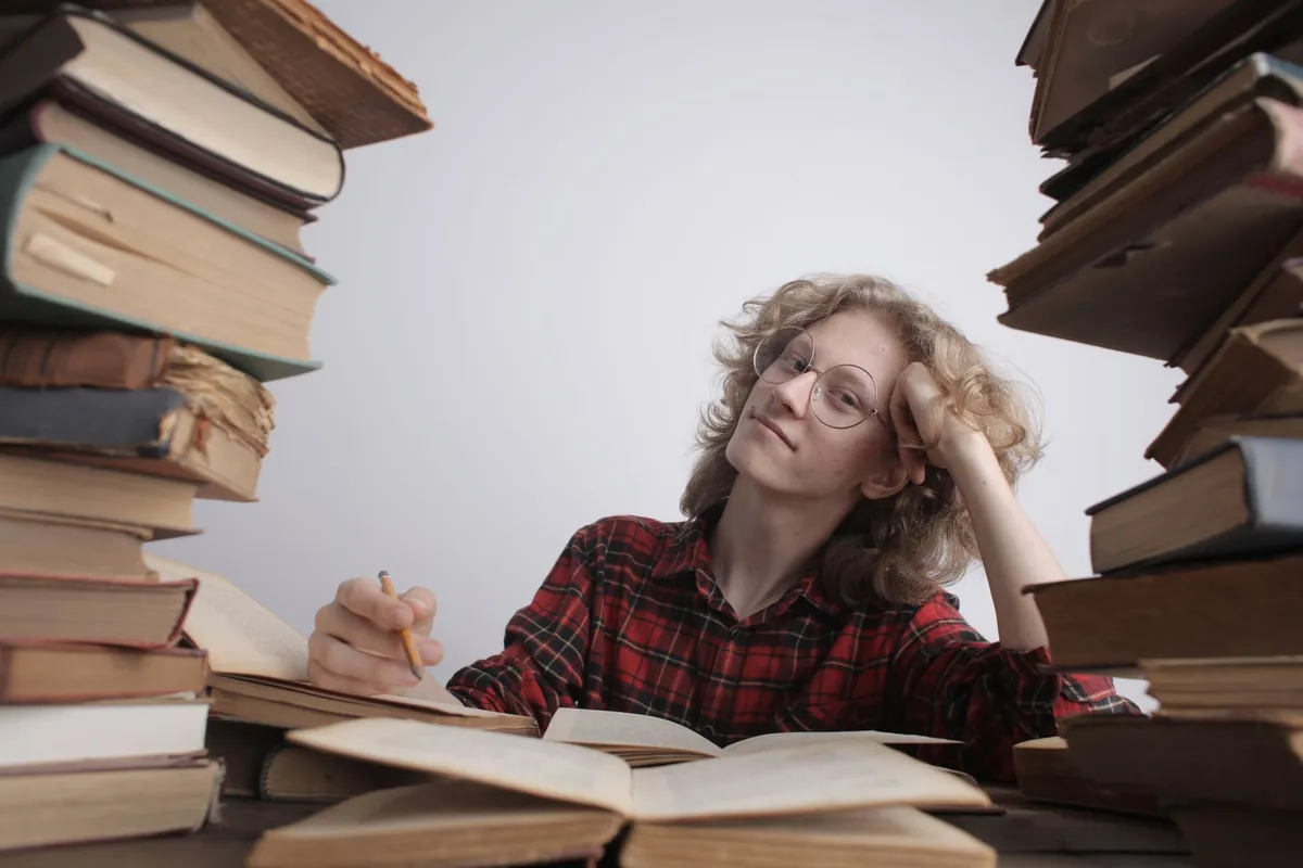 A young woman studying intensely surrounded by large stacks of books in a library setting.
